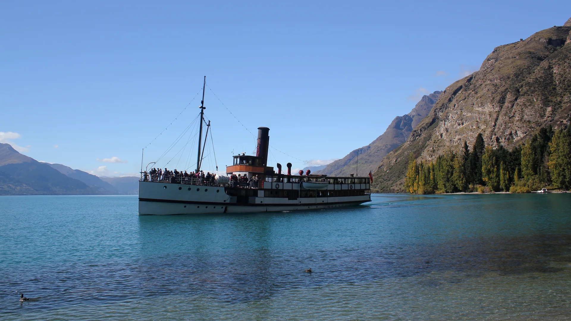 The TSS Earnslaw steamship, its funnel and rigging whole and clear, crossing Lake Wakatipu toward Walter Peak with the Remarkables behind